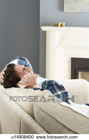 Stock Image - Man Relaxing Sitting On Sofa At Home Talking On Phone. Fotosearch