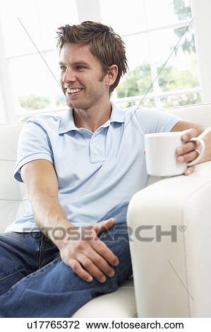 Stock Image - Man Sitting On Sofa Drinking Coffee Relaxing At Home. Fotosearch