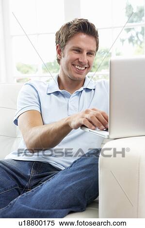 Stock Photography - Man Sitting On Sofa Using Laptop At Home. Fotosearch