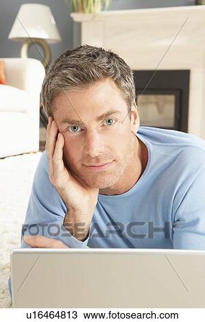 Stock Image - Man Using Laptop Relaxing Laying On Rug At Home . Fotosearch
