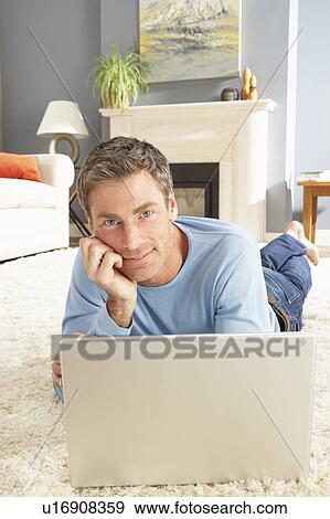 Stock Photo - Man Using Laptop Relaxing Laying On Rug At Home . Fotosearch