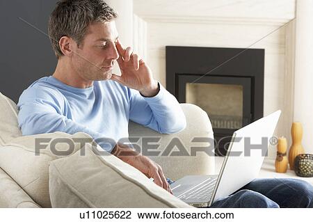 Stock Image - Man Using Laptop Relaxing Sitting On Sofa At Home . Fotosearch