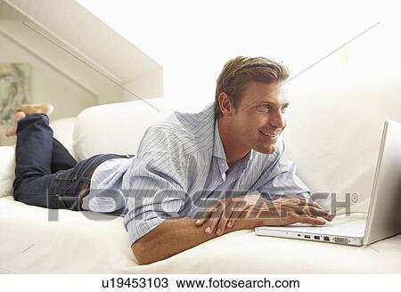 Stock Image - Man Using Laptop Relaxing Sitting On Sofa At Home. Fotosearch