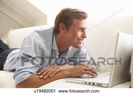 Stock Image - Man Using Laptop Relaxing Sitting On Sofa At Home. Fotosearch