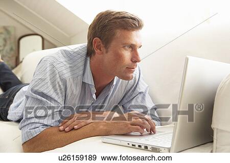 Stock Photo - Man Using Laptop Relaxing Sitting On Sofa At Home. Fotosearch