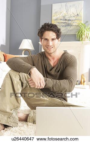 Stock Photo - Man Using Laptop Relaxing Sitting On Rug At Home. Fotosearch