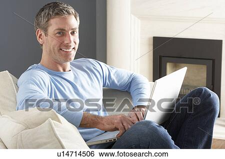 Stock Photograph - Man Using Laptop Relaxing Sitting On Sofa At Home . Fotosearch