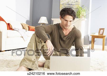 Stock Photograph - Man Using Laptop Relaxing Sitting On Rug At Home . Fotosearch