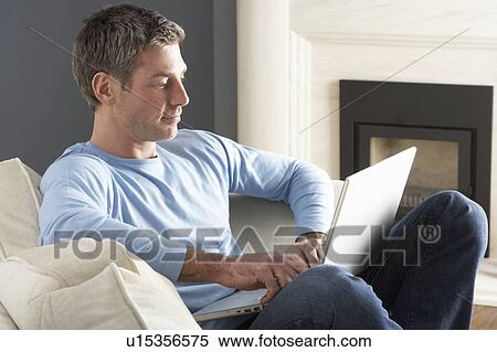 Stock Photography - Man Using Laptop Relaxing Sitting On Sofa At Home . Fotosearch