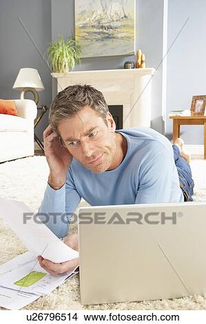 Man Using Laptop To Manage Household Bills Laying On Rug At Home View Large Photo Image Picture - Man Using Laptop To Manage Household Bills Laying On Rug At Home . Fotosearch