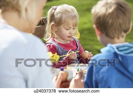 Stock Photo - Mother And Children Decorating Easter Eggs On Table Outdoors . Fotosearch