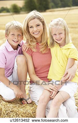 Stock Image - Mother And Children Sitting On Straw Bales In Harvested Field. Fotosearch