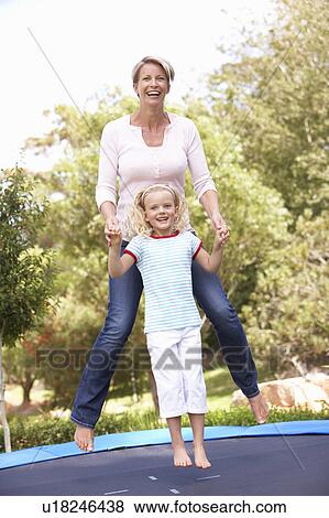 Stock Photo - Mother And Daughter Jumping On Trampoline In Garden. Fotosearch