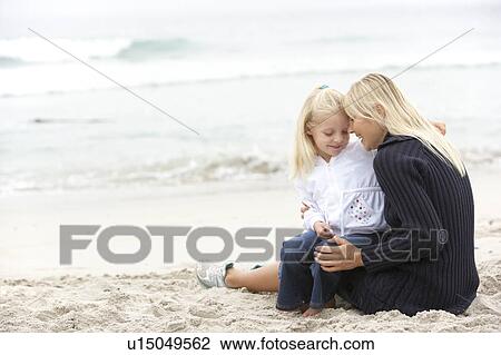 Stock Image - Mother And Daughter On Holiday Sitting On Winter Beach. Fotosearch