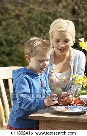 Stock Photography - Mother And Son Decorating Easter Eggs On Table Outdoors . Fotosearch