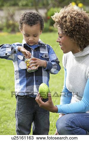 Stock Image - Mother Helping Son To Unwrap Chocolate Easter Egg. Fotosearch