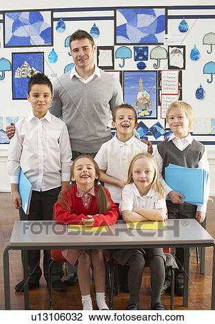 Stock Image - Portrait Of Group Of Primary Schoolchildren And Teacher Sitting At Desk In Classroom. Fotosearch