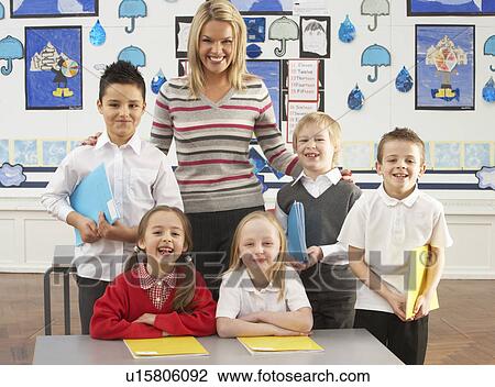 Stock Image - Portrait Of Group Of Primary Schoolchildren And Teacher Sitting At Desk In Classroom. Fotosearch