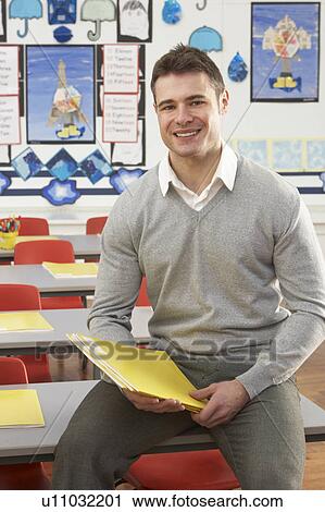 Stock Image - Portrait Of Male Teacher Sitting At Desk In Classroom. Fotosearch