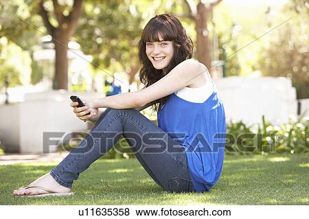 Stock Photo - Portrait Of Teenage Girl Sitting In Park Using Mobile Phone. Fotosearch