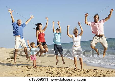 Stock Image - Portrait Of Three Generation Family On Beach Holiday Jumping In Air. Fotosearch