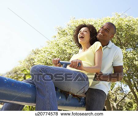 Stock Photo - Portrait Of Young Couple Riding On SeeSaw In Park. Fotosearch