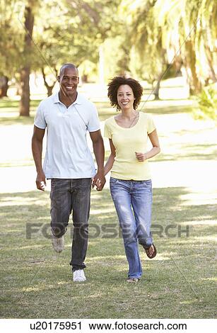 Stock Image - Portrait Of Young Couple Running Through Park. Fotosearch