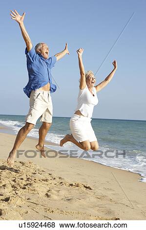 Stock Photo - Senior Couple Enjoying Beach Holiday Jumping In Air. Fotosearch