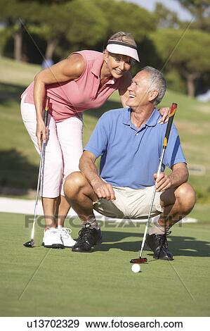 Stock Photo - Senior Couple Golfing On Golf Course Lining Up Putt On Green. Fotosearch