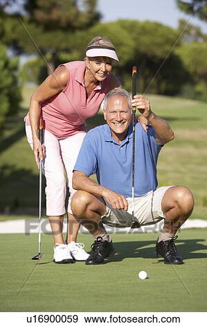 Stock Photo - Senior Couple Golfing On Golf Course Lining Up Putt On Green. Fotosearch
