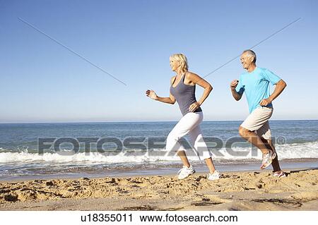 Stock Image - Senior Couple In Fitness Clothing Running Along Beach. Fotosearch