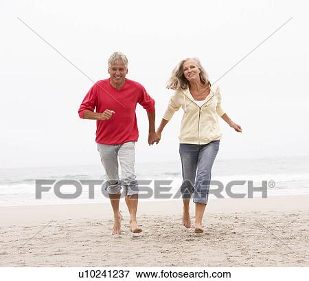 Stock Photo - Senior Couple On Holiday Running Along Winter Beach. Fotosearch