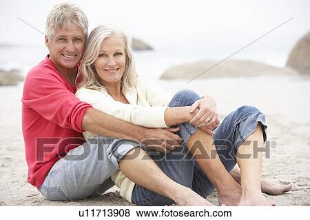 Stock Photo - Senior Couple On Holiday Sitting On Winter Beach. Fotosearch