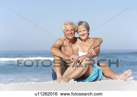 Stock Photograph - Senior Couple On Holiday Sitting On Sandy Beach. Fotosearch
