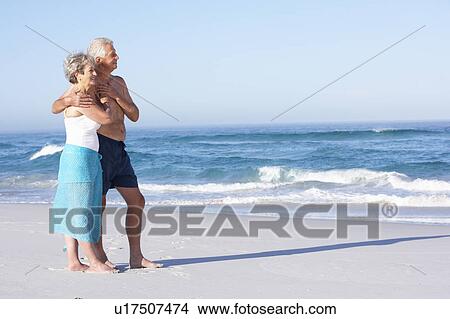 Picture - Senior Couple On Holiday Walking Along Sandy Beach. Fotosearch