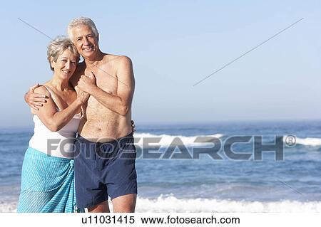 Stock Photography - Senior Couple On Holiday Walking Along Sandy Beach. Fotosearch