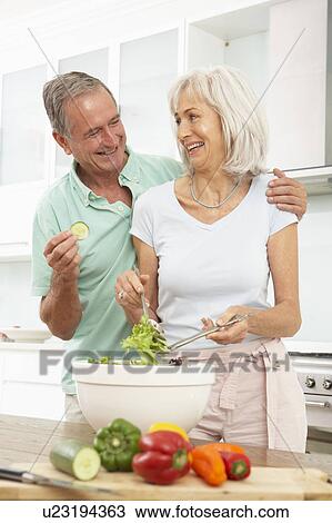 Stock Image - Senior Couple Preparing Salad In Modern Kitchen. Fotosearch