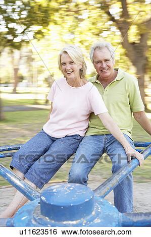 Stock Photograph - Senior Couple Riding On Roundabout In Park. Fotosearch