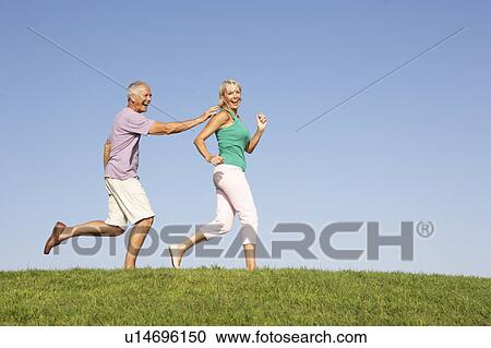 Stock Image - Senior couple running though field. Fotosearch