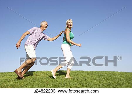 Stock Image - Senior couple running though field. Fotosearch