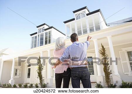 Stock Image - Senior Couple Standing Outside Dream Home. Fotosearch