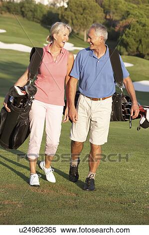 Stock Photography - Senior Couple Walking Along Golf Course Carrying Bags. Fotosearch