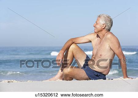 Stock Image - Senior Man On Holiday Sitting On Sandy Beach. Fotosearch