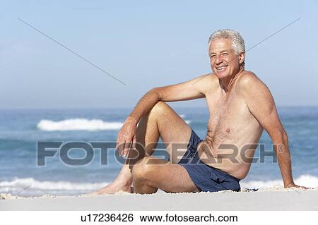 Stock Photograph - Senior Man On Holiday Sitting On Sandy Beach. Fotosearch