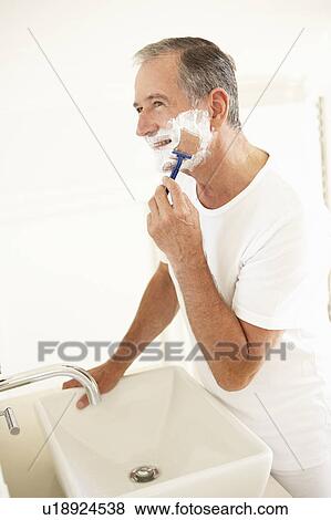 Stock Photo - Senior Man Shaving In Bathroom Mirror. Fotosearch