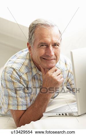 Senior Man Using Laptop Relaxing Sitting On Sofa At Home View Large Photo Image Picture - Senior Man Using Laptop Relaxing Sitting On Sofa At Home. Fotosearch