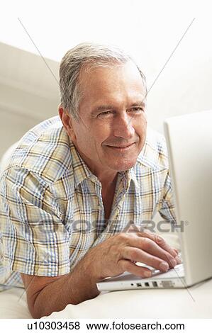 Stock Photo - Senior Man Using Laptop Relaxing Sitting On Sofa At Home. Fotosearch