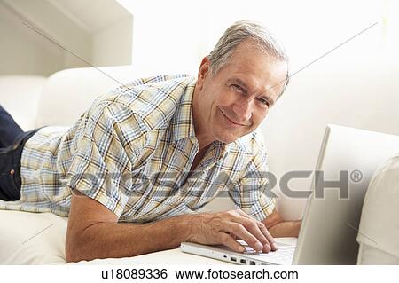 Stock Photograph - Senior Man Using Laptop Relaxing Sitting On Sofa At Home. Fotosearch