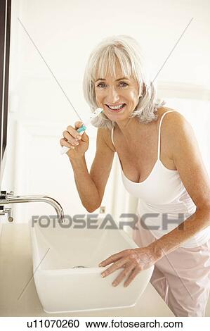 Stock Image - Senior Woman Brushing Teeth In Bathroom. Fotosearch