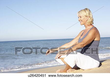 Stock Image - Senior Woman In Fitness Clothing Meditating On Beach. Fotosearch